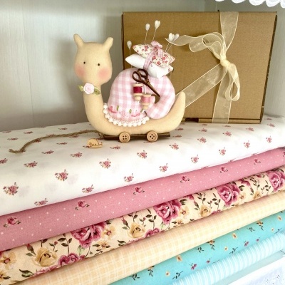 Caracol decorativo tecido bege com casco xadrez rosa sobre tecidos coloridos florais e caixa presente