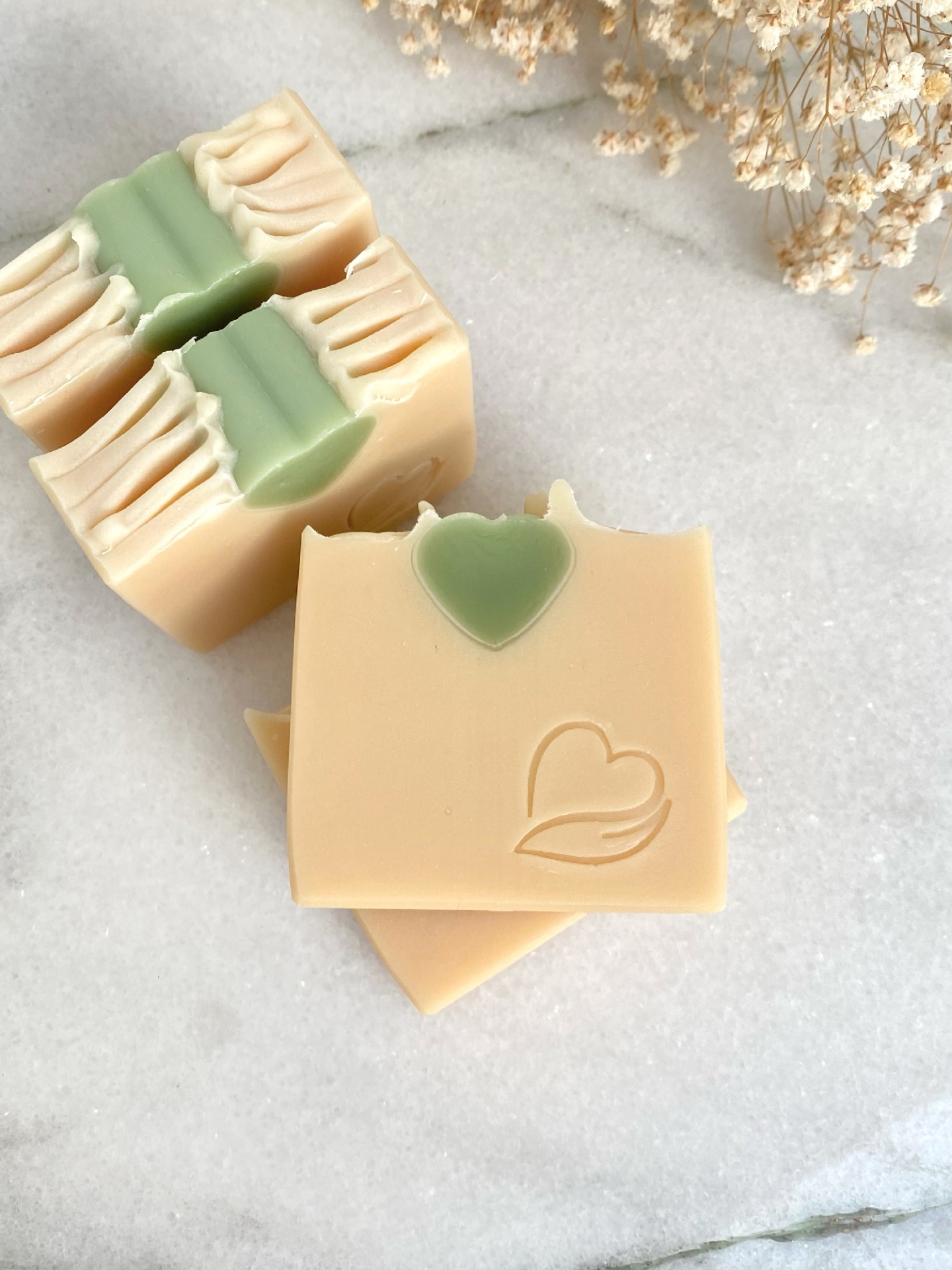 Sabonete Natural Coco fresh Sabonetes quadrados bege com detalhe verde e relevo de coração, sobre superfície clara com flores secas