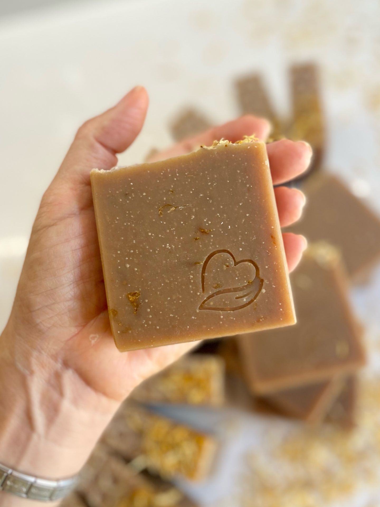 Sabonete natural de calêndula, aveia e mel Sabonete castanho quadrado com partículas e símbolo de coração