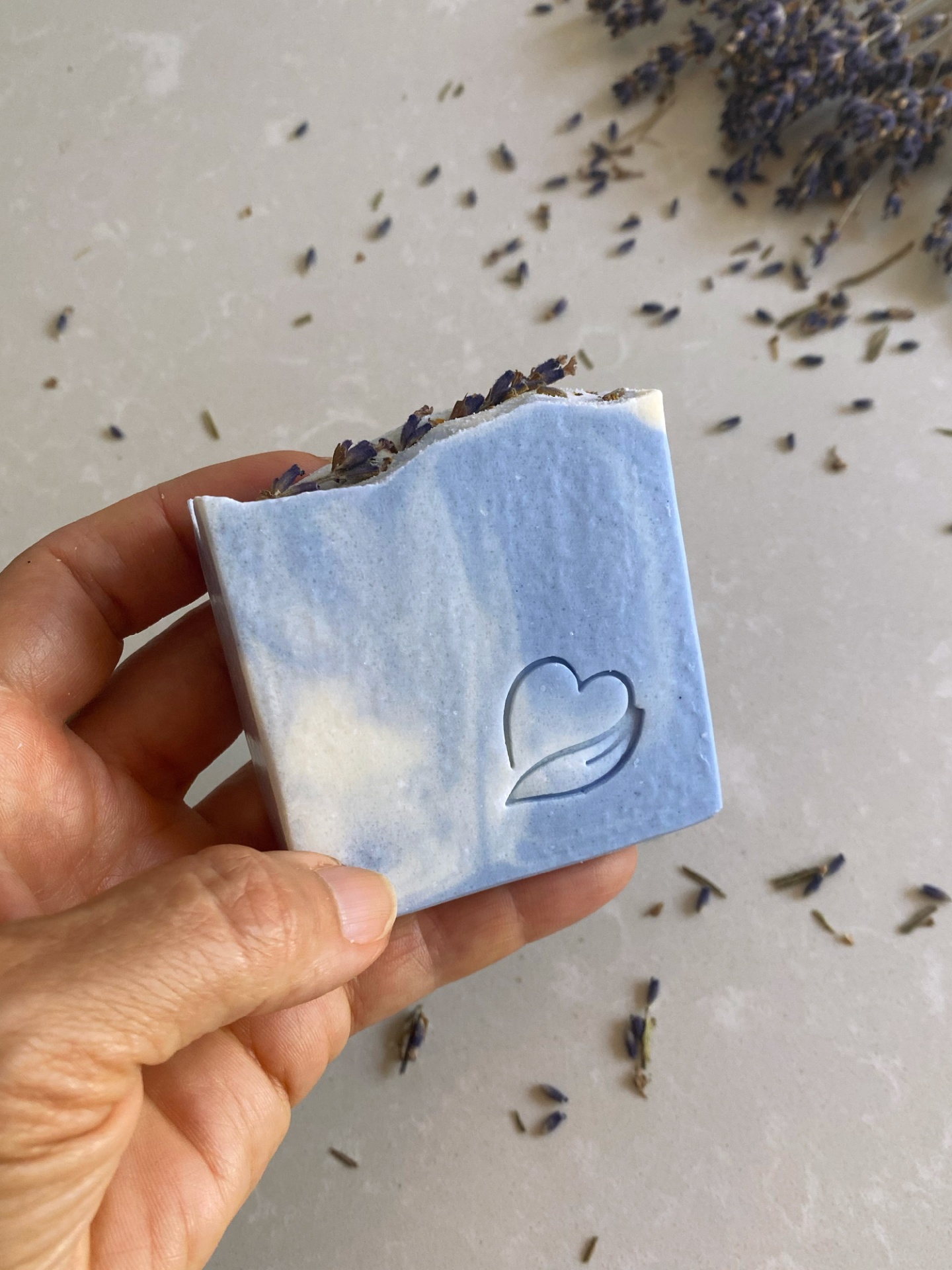 Sabonete natural de lavanda Sabonete azul e branco com flores secas de lavanda e gravação de coração, segurado por uma mão