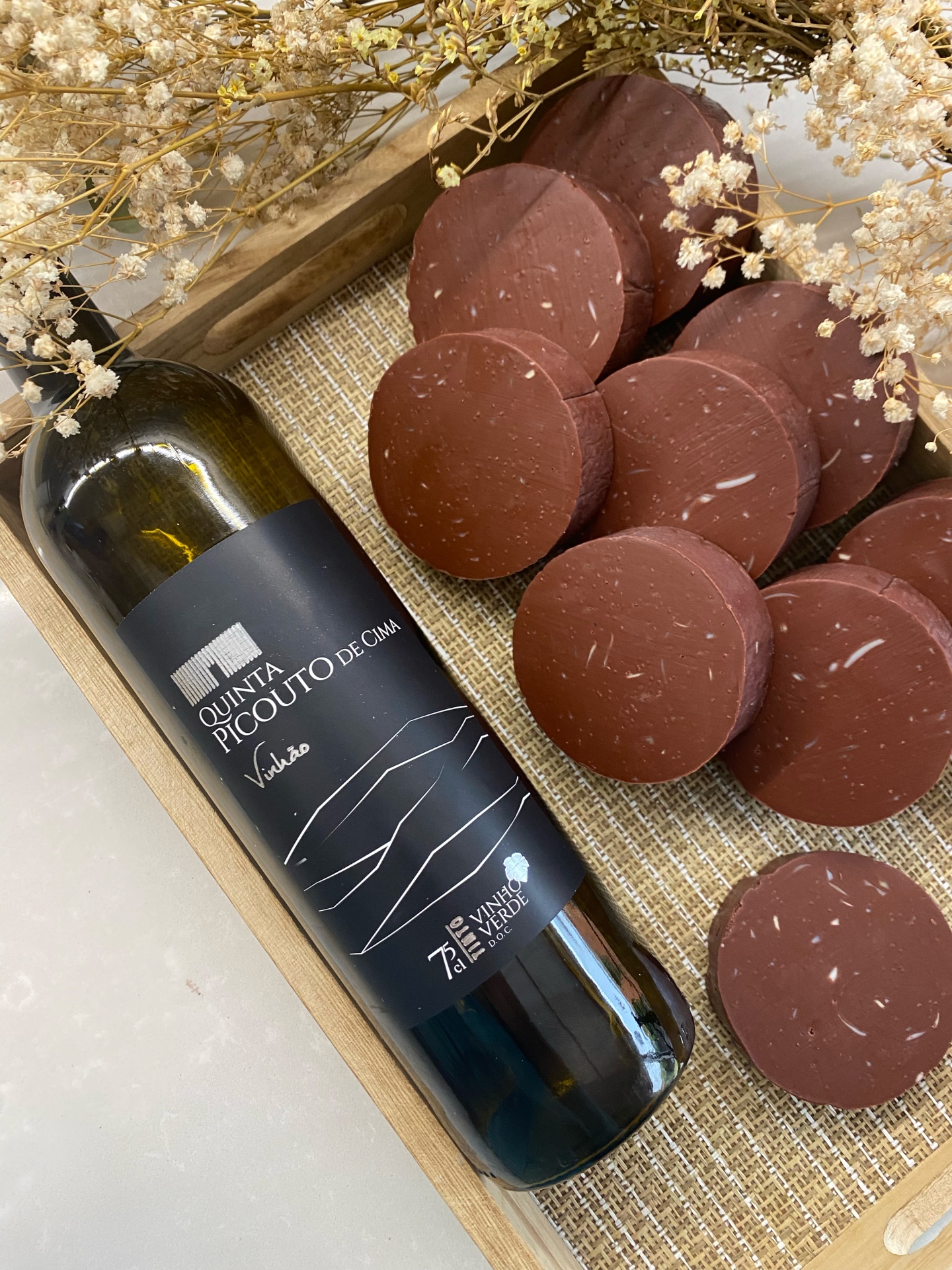 Workshop Sabonetes Naturais de Vinho Garrafa de vinho verde Quinta Picouto de Cima e fatias de queijo castanho em bandeja de madeira com flores secas