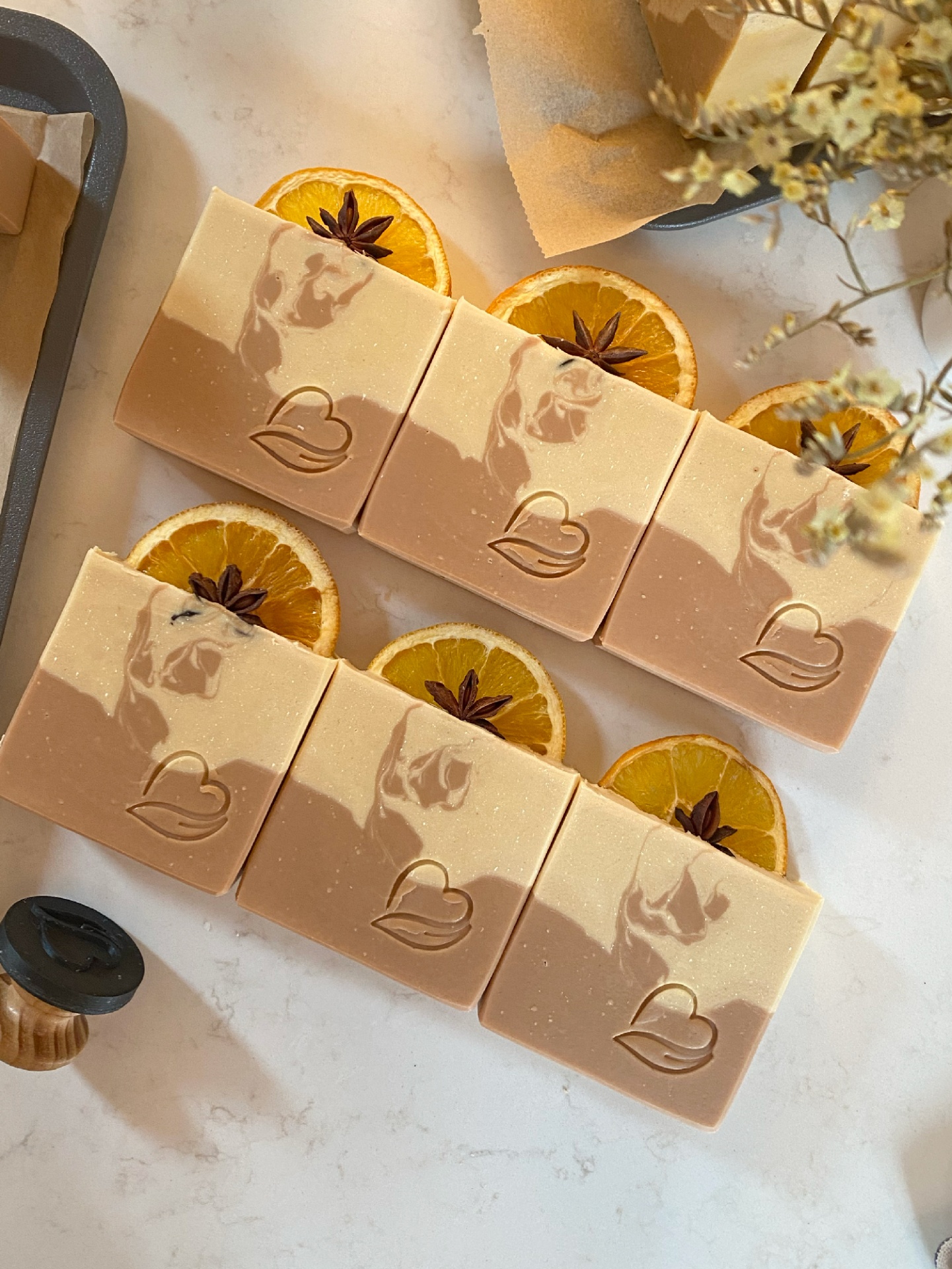 Sabonete Natural Laranja Anis Seis sabonetes retangulares bege com coração gravado em cima de fatias de laranja secas e anis-estrelado