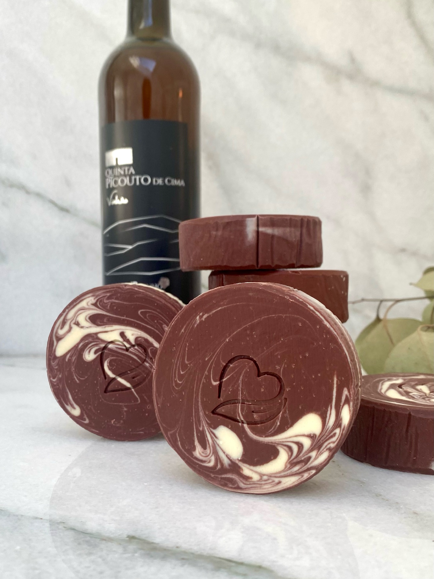 Sabonete natural de vinho Tinto Sabonetes redondos com padrão castanho e branco e garrafa de vidro castanha com rótulo preto.