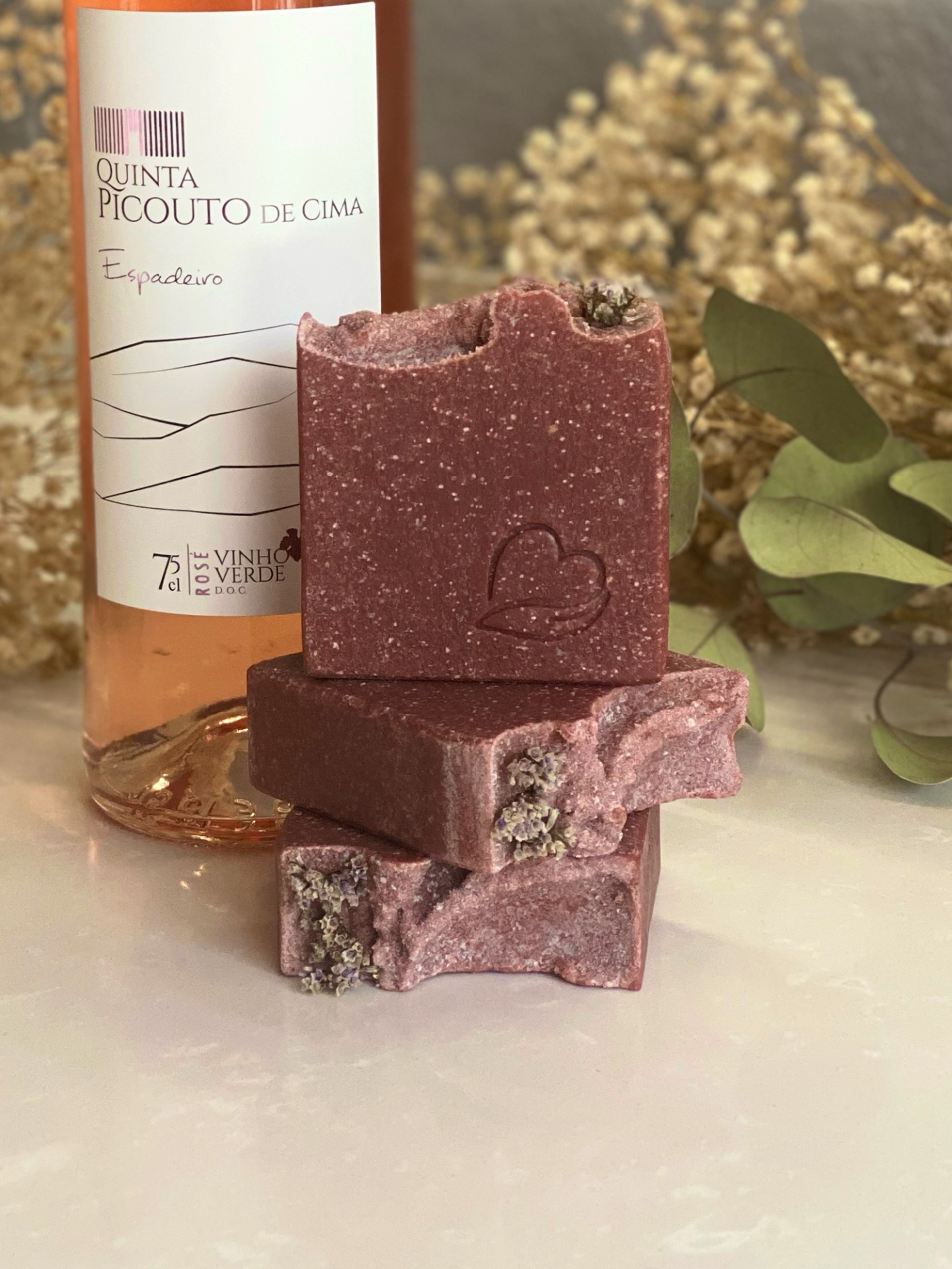Sabonete natural de vinho rosé Garrafa de vinho rosé e sabonetes artesanais rosa avermelhado com textura granulada e detalhe floral