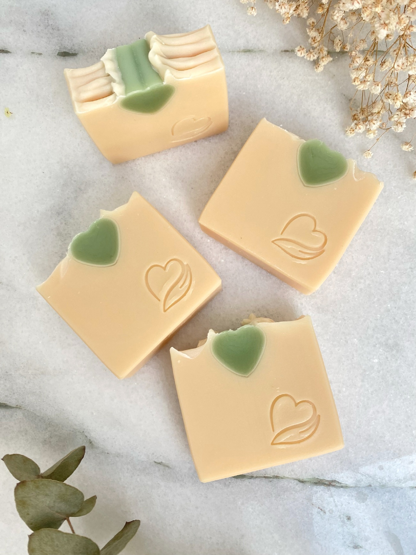 Sabonete Natural Coco fresh Quatro sabonetes quadrados bege com coração verde e símbolo gravado sobre mármore branco.