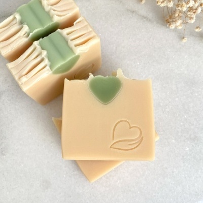 Sabonetes quadrados bege com detalhe verde e relevo de coração, sobre superfície clara com flores secas