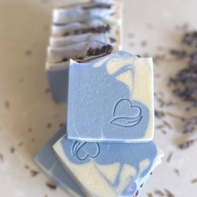 Barras de sabão azul e creme com desenho de coração e folha e flores secas em fundo neutro