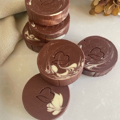 Seis sabonetes redondos castanhos com manchas brancas e coração gravado no topo sobre superfície clara