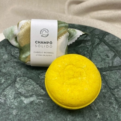 Champô sólido amarelo e embalagem de tecido sobre prato verde de mármore