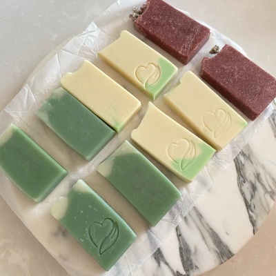 Sabonetes artesanais verdes, bege e vermelhos em papel sobre mármore.