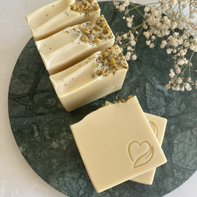 Sabonetes sólidos creme com flores secas e sementes decorativas, em prato verde, junto a flores secas brancas.