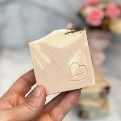 Sabonete artesanal bege com relevo de coração segurado por uma mão