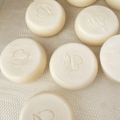 Sabonetes brancos redondos com desenho de coração e folha sobre superfície texturizada