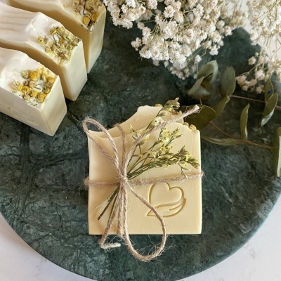 Sabonetes artesanais creme com flores secas, decorados e apresentados numa placa de pedra verde.