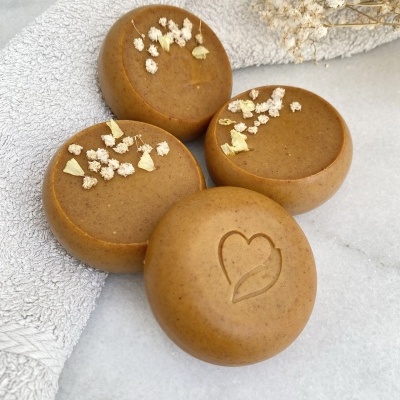 Quatro sabonetes redondos castanhos com flores secas, sobre toalha cinza clara