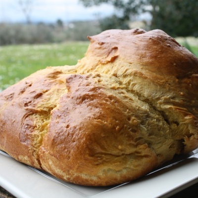 Pão caseiro redondo com crosta dourada num prato branco ao ar livre