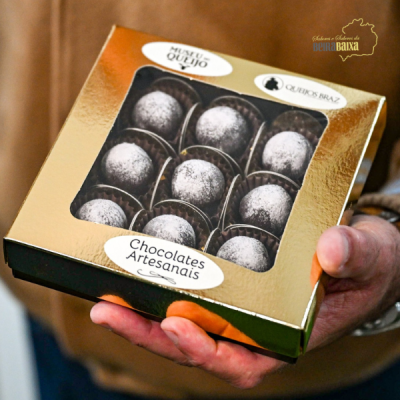 Caixa dourada com chocolates artesanais redondos visíveis pela janela de plástico