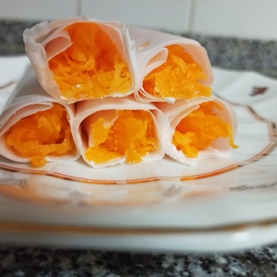 Cinco rolinhos de papel translúcido com recheio laranja num prato decorado branco.