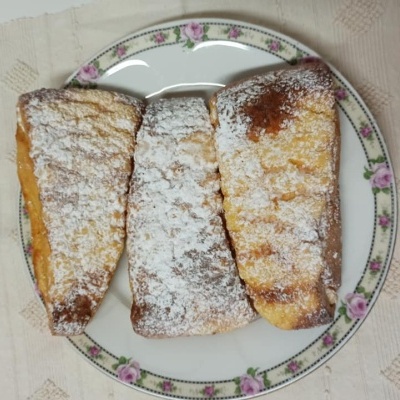 Três pastéis polvilhados com açúcar em pó num prato floral sobre pano branco