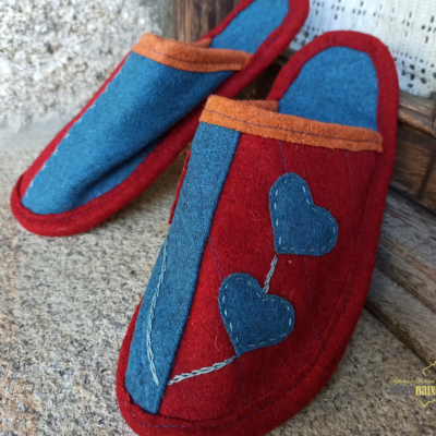 Chinelos de pano vermelhos e azuis com corações azuis junto a porta de madeira e parede de tijolos