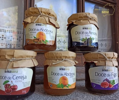 Cinco frascos de compotas artesanais com etiquetas e tampas de papel castanho, em superfície de pedra.