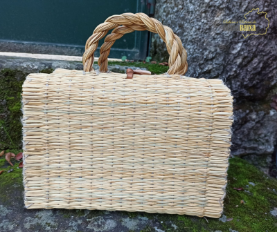 Mala de mão em fibras naturais com alças trançadas sobre pedra com musgo