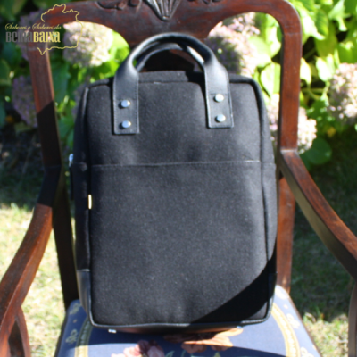 Mochila preta de tecido com alças reforçadas numa cadeira de madeira ao ar livre