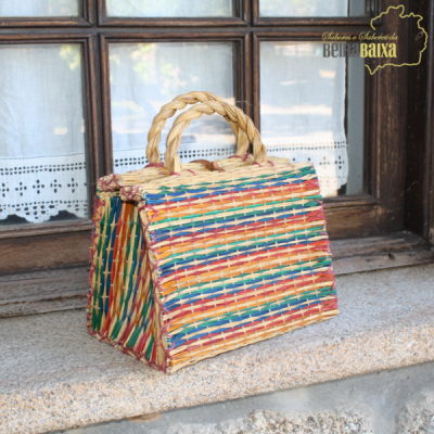 Bolsa de palha colorida com alças em pedra junto a janela com cortinas brancas
