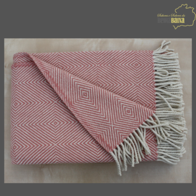 Manta vermelha e branca com padrão geométrico e franjas, sobre superfície bege com texto no canto superior direito