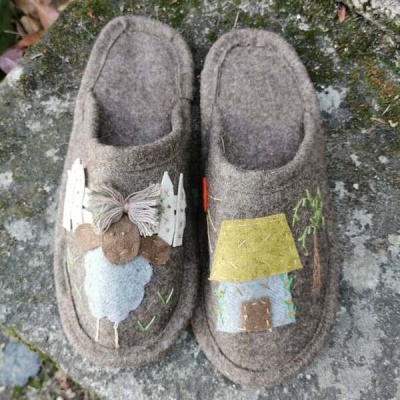 Chinelos de feltro castanhos com desenhos bordados de ovelha e casa sobre pedra musgosa