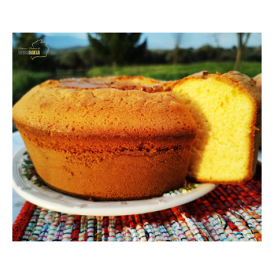 Bolo amarelo caseiro fatiado num prato branco com padrão floral em tecido colorido, com fundo natural.