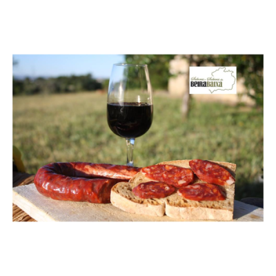 Taça de vinho tinto, linguiça fumada e pão com chouriço numa tábua de madeira ao ar livre