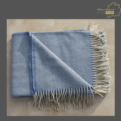 Manta azul com padrão geométrico e franjas brancas sobre superfície clara