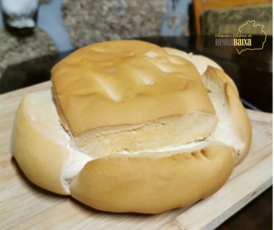 Pão tipo bola dourado com vincos numa tábua de madeira