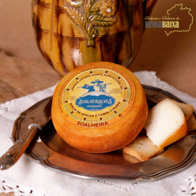 Queijo Soalheiralves curado em prato metálico com faca e peça cerâmica ao fundo.