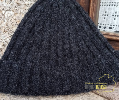 Gorro de malha cinzento escuro com padrão de trança em fundo de pedra e madeira