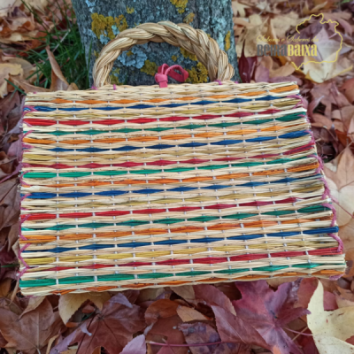 Mala de mão trançada colorida com cabo trançado colocada sobre folhas secas