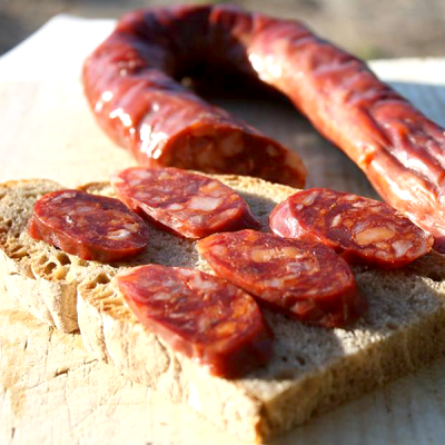 Chouriço cortado em rodelas sobre pão rústico em tábua de madeira