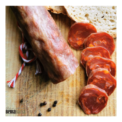 Linguiça embutida fatiada e inteira sobre tábua de madeira com pão e pimenta preta