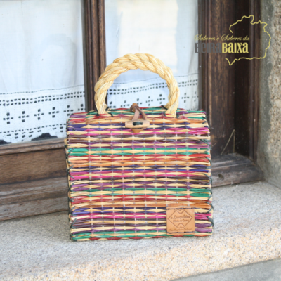 Bolsa quadrada colorida de palha com alça e etiqueta de couro, sobre peitoril de pedra