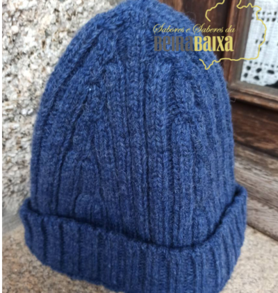 Gorro azul em malha com padrão de trança colocado junto a uma janela de madeira