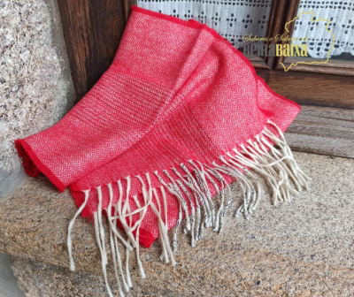 Lenço vermelho com franjas brancas numa superfície de pedra junto a janela de madeira