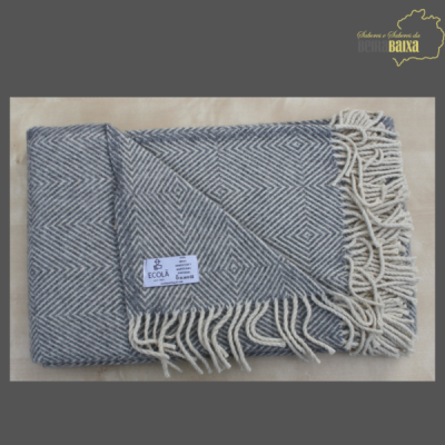 Manta cinza com padrão geométrico e franjas brancas, etiqueta ECOLÃ, sobre fundo bege com marca d'água no canto superior direito.
