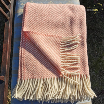 Manta rosa claro com franjas creme sobre almofada azul ao ar livre