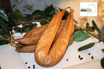 Chouriças castanhas alaranjadas em prato branco com folhas verdes e pimenta, logotipo SABORES DA BEIRA BAIXA