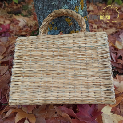 Cesto de verga trançada com pega dupla sobre folhas secas