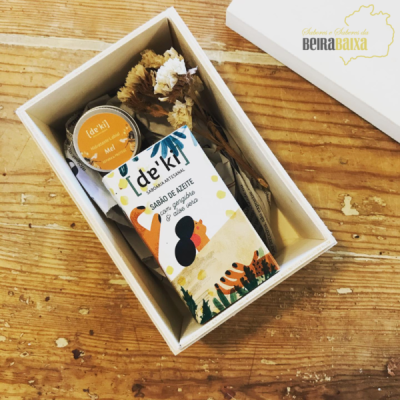 Caixa branca com sabonete, frasco de mel e flores secas em fundo de madeira