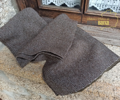 Cachecol tricotado cinza e castanho sobre bancada de pedra em frente a janela de madeira com cortinas de renda