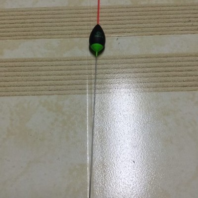Boia de pesca preta com base verde e antena vermelha sobre chão de azulejos claros