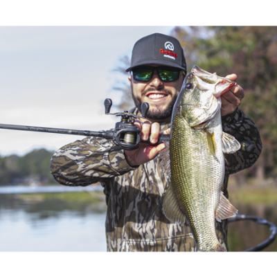 Homem a pescar segurando peixe grande e cana de pesca junto a lago